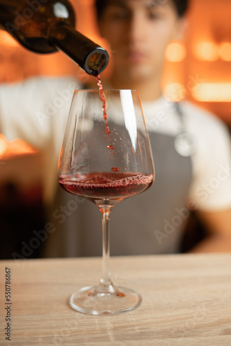 Bartender pouring red wine from a bottle in a wine glass, selective focus on a wine glass.