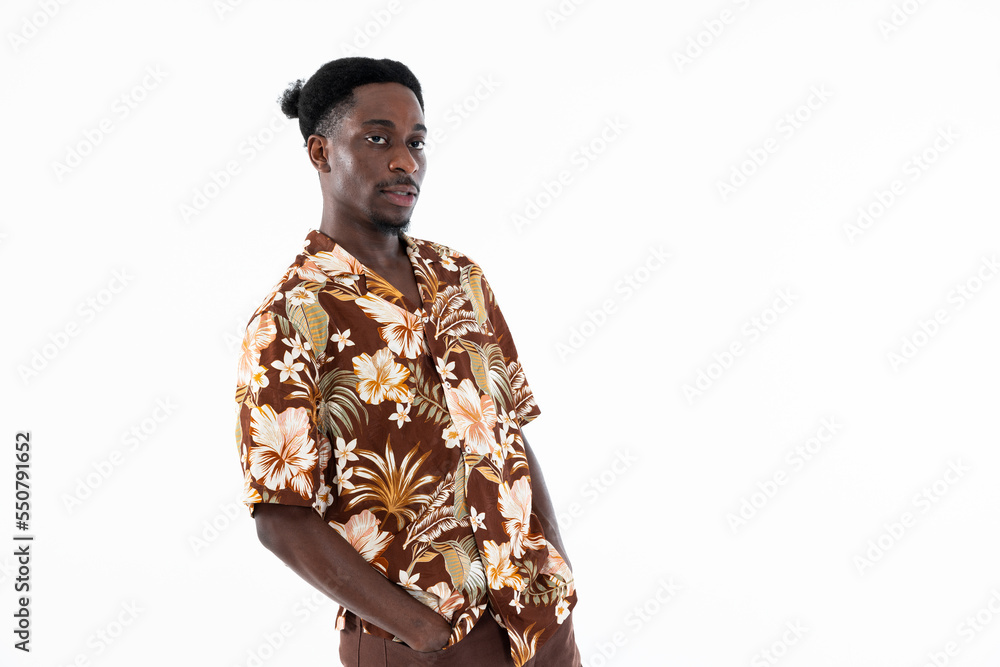 Handsome african american man with funny hairstyle holding hands in pocket looking at camera. Fashionable guy wearing colorful shirt and brown pants.