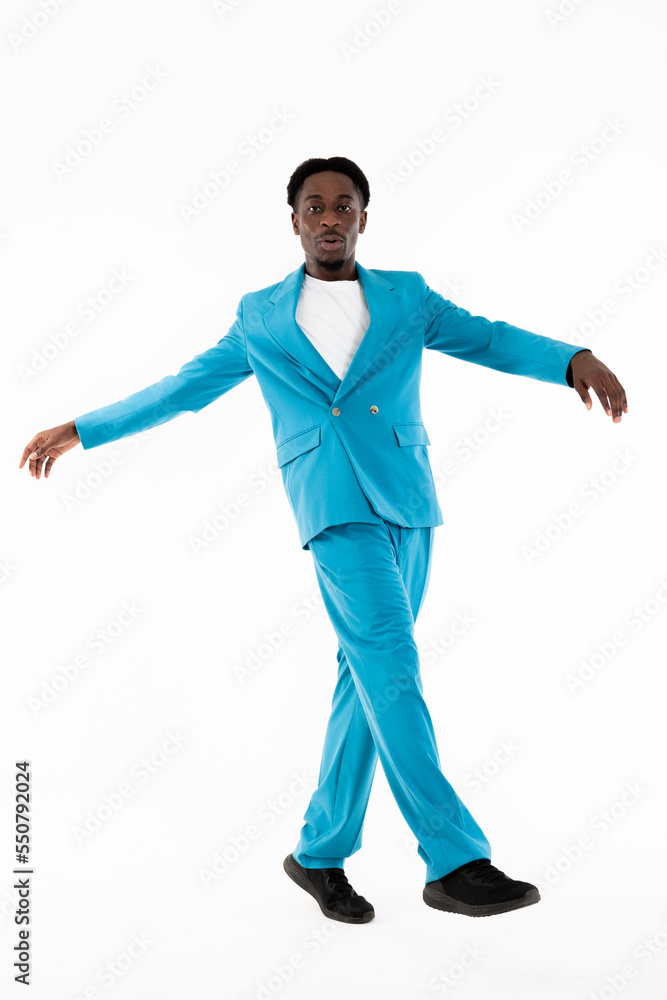 Good-looking african american man looking at camea posing for fashion magazine wearing smart casual blue suit and white t-shirt spreading hands to the side crossing legs. Dark skinned model good mood.