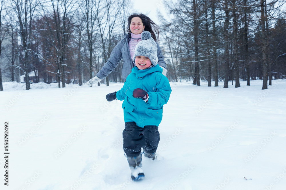 Laughing boy with his mother run in the snow. Family on a walk in winter.