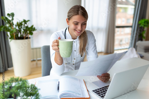 Doctor professional female doctor wearing uniform taking notes in medical journal, filling documents, patient illness history, looking at laptop screen, student watching webinar
