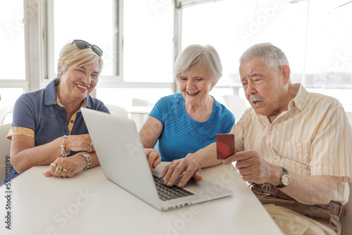 tre anziani seduti al bar fanno un ordine con il computer attraverso la carta di credito  photo