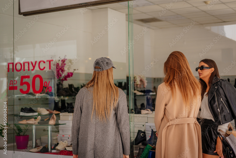 A back view photo of three girls looking through the shop window. They are about to buy new shoes