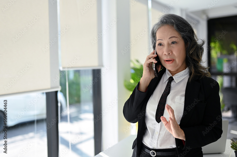 Professional Asian senior businesswoman talking on the phone with her business partner. Professional Asian senior businesswoman talking on the phone with her business partner.