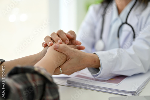 Female doctor holds her young patient s hands  giving support and reassuring her during checkup