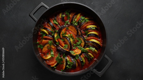 Layered ratatouille in a baking dish, slices of zucchini, red bell pepper, chili, yellow squash, eggplant, olive oil, parsley and garlic