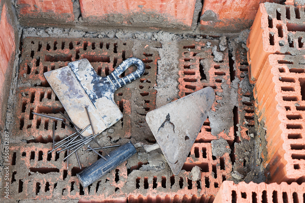 Construction tool for laying bricks and blocks. Bricklayer's tools - hammer, spatula, trowel, gloves. Hand tools on the background of brickwork.
