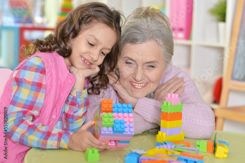 Cute girl and grandmother playing with colorful plastic blocks