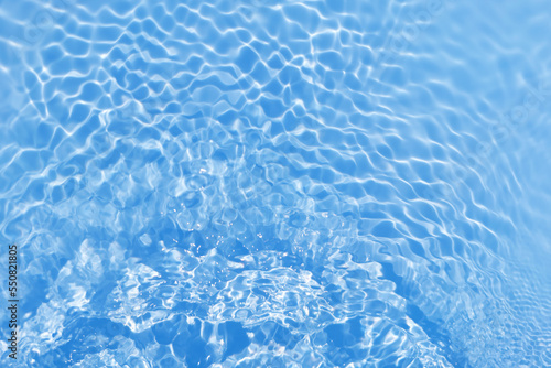 Defocus blurred transparent blue colored clear calm water surface texture with splashes and bubbles. Trendy abstract nature background. Water waves in sunlight with copy space. Blue watercolor shining