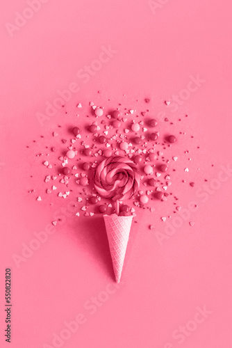 Trendy color of the year 2023. Ice cream waffle cone with lollipop on stick, scattering of sweets and confectionery topping toned with vava magenda photo