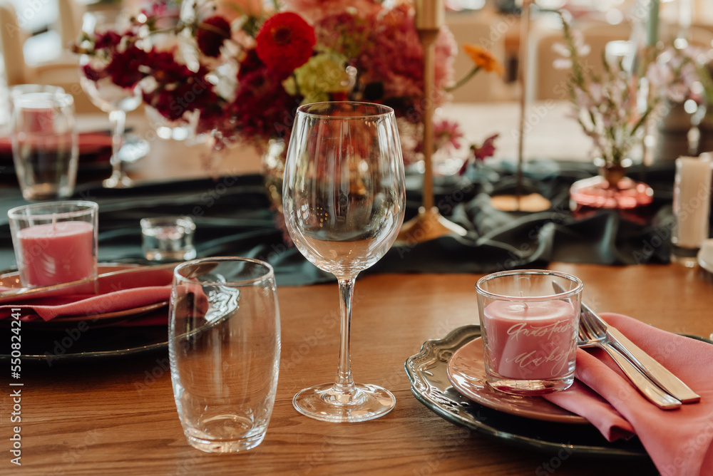 Table setting with cutlery and glass for two persons close-up. On a wooden table are a crystal goblet and a glass next to which are green plates with silver knives and forks