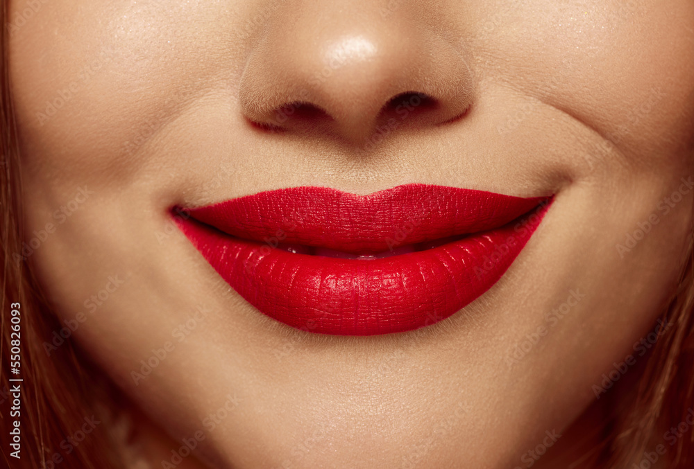 Obraz premium Closeup view of female mouth with bright red lipstick. Beautiful light smile of young woman with perfect face skin. Facial expressions