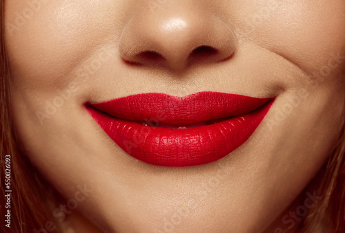 Closeup view of female mouth with bright red lipstick. Beautiful light smile of young woman with perfect face skin. Facial expressions