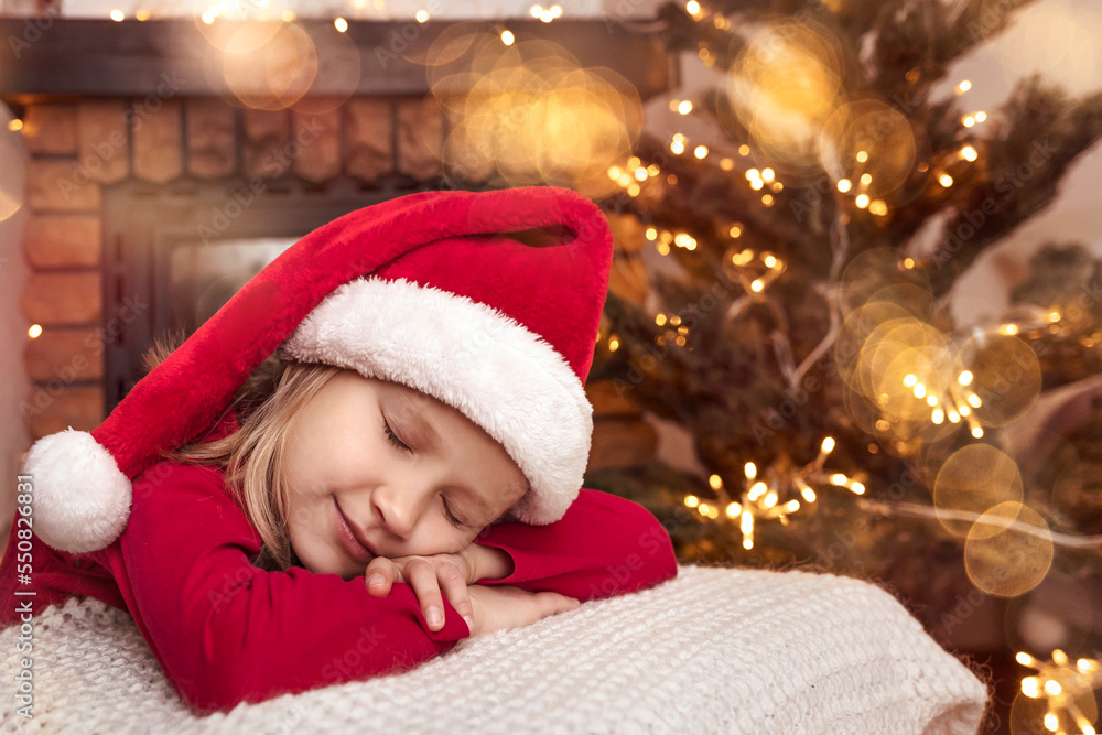 Christmas and New Year Holiday Coming Concept. Christmas Kid Girl in Red Santa Hat is Sleeping Waiting for Santa in Christmas Home. Space for text. Christmas and New Year Holiday Coming Concept. Christmas Kid Girl in Red Santa Hat is Sleeping Waiting for Santa in Christmas Home. Space for text.