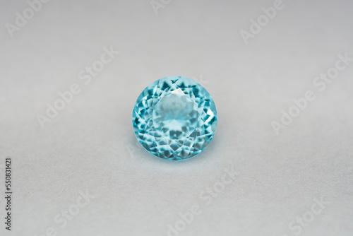 Deep sky blue colored topaz or swiss blue topaz gemstone setting on light gray background position center. Transparent colorful clean round faceted loose gem piece for making jewelry. Gemology theme
