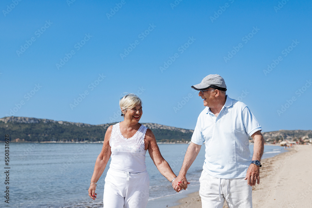 coppia di anziani coniugi si abbraccia affettuosamente mentre cammina lungo la battigia di una spiaggia coppia di anziani coniugi si abbraccia affettuosamente mentre cammina lungo la battigia di una spiaggia
