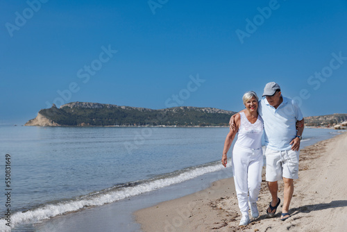 coppia di anziani coniugi si abbraccia affettuosamente mentre cammina lungo la battigia di una spiaggia  © alex.pin