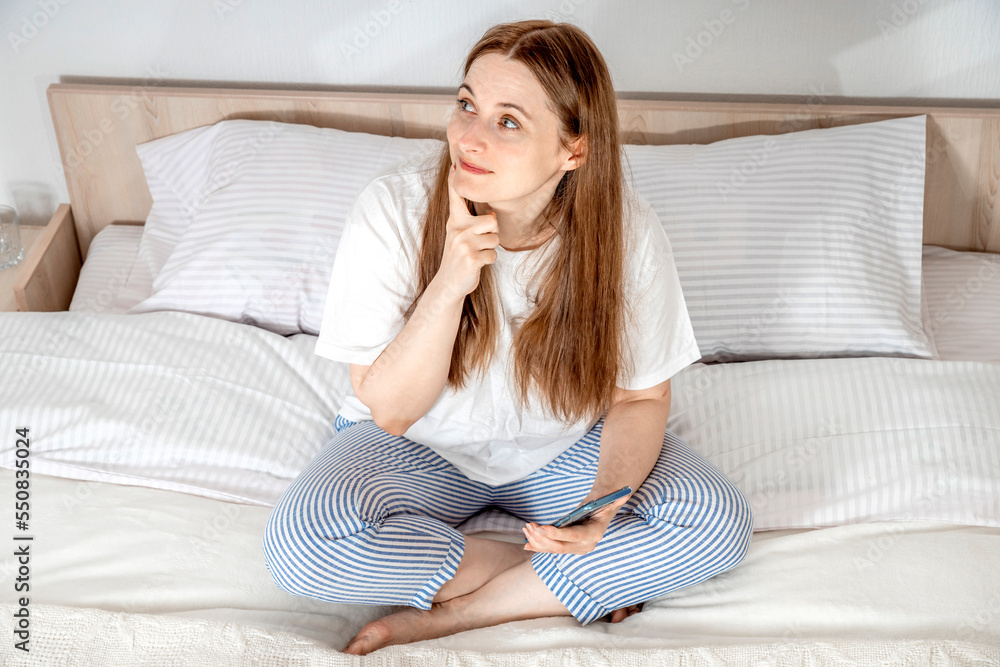 Woman with smartphone in bed at home or hotel in the morning. Lady relaxing in a nightgown. Girl wearing nightie on clean white bedding, cozy blanket Woman with smartphone in bed at home or hotel in the morning. Lady relaxing in a nightgown. Girl wearing nightie on clean white bedding, cozy blanket
