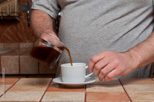 Male hands pour coffee into a coffee cup standing on a tiled kitchen table