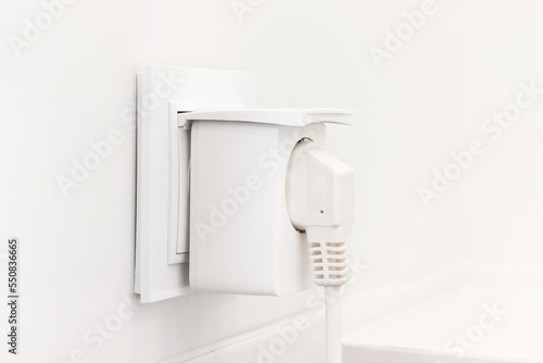 White european electrical outlet with smart plug inserted into it on modern bright bathroom with white tiled wall