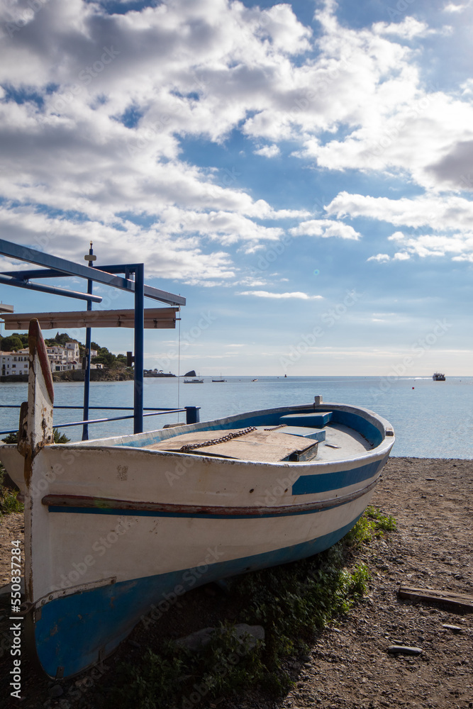 Barca azul y blanca estacionada en la arena de la playa del pueblo catalán de Cadaqués con el mar de fondo bajo un cielo azul con nubes.