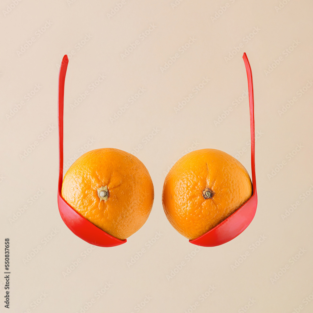 Breast and bra made with oranges or tangerines in bold red ladles on  isolated beige background. Minimal aesthetic abstract idea of boobs.  Creative food concept with citrus fruit and kitchen equipment. Photos