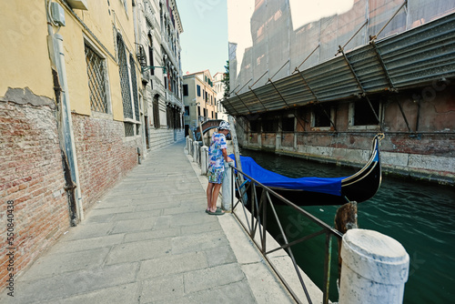 Boy stand near canal with covered gondola in Venice  Italy.