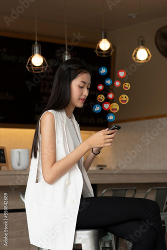 Asian woman enjoy using mobile phone addiction to technology trends following and chatting with icons on social networks in coffee shop. Social medias and technology concept.