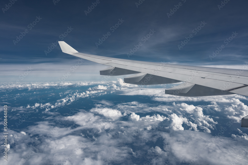 Wing of airplane above flat fluffy clouds surface with soft evening sunlight. Copy space.