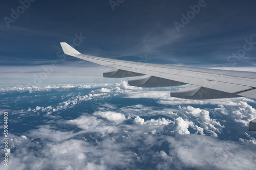 Wing of airplane above flat fluffy clouds surface with soft evening sunlight. Copy space.
