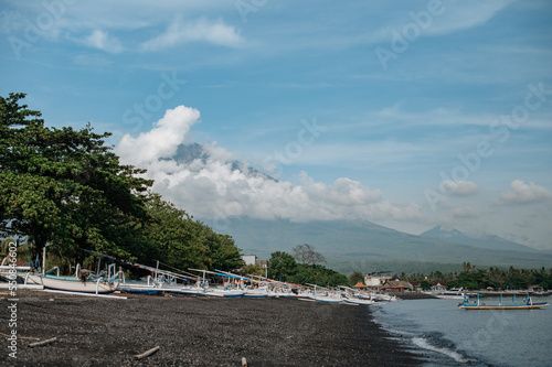 Aerial view of Amed beach in Bali, Indonesia. Traditional fishing boats called jukung on the black sand beach and Mount Agung volcano photo