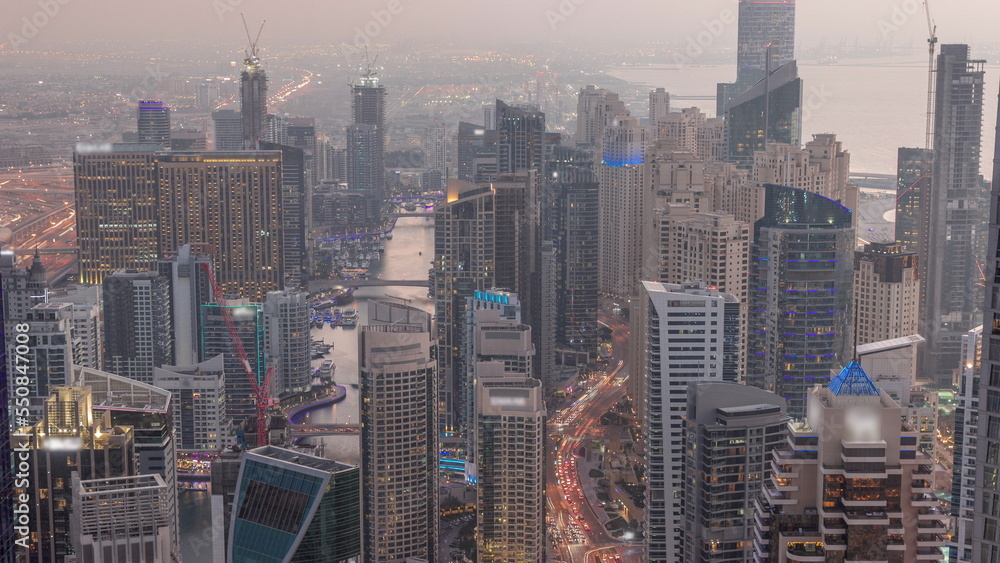 Obraz premium Skyline view of Dubai Marina showing canal surrounded by skyscrapers along shoreline day to night timelapse. DUBAI, UAE