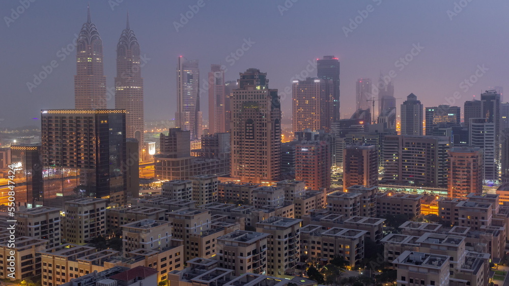 Obraz premium Skyscrapers in Barsha Heights district and low rise buildings in Greens district aerial night to day timelapse.