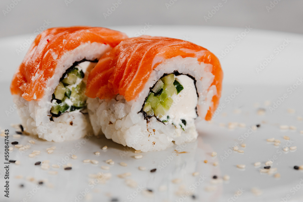 Two portions of sushi with salmon and cucumber on a white plate. Two portions of sushi with salmon and cucumber on a white plate.