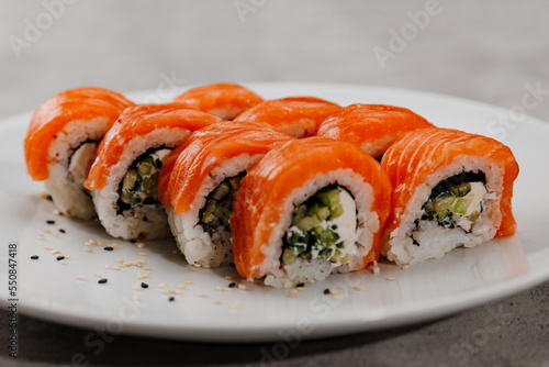 Eight servings of sushi with salmon and cucumber on a white plate. 