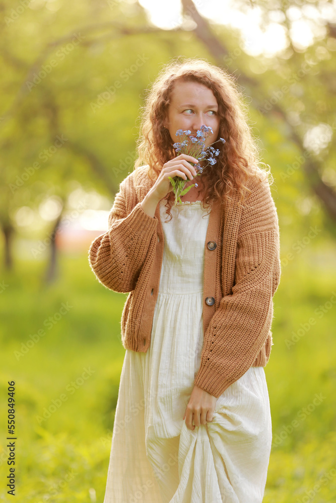 young woman plucks wild blue flowers in the green park on summer sunny day. girl with curly hair in dress makes bouquet of beautiful flowers. vertical photo young woman plucks wild blue flowers in the green park on summer sunny day. girl with curly hair in dress makes bouquet of beautiful flowers. vertical photo