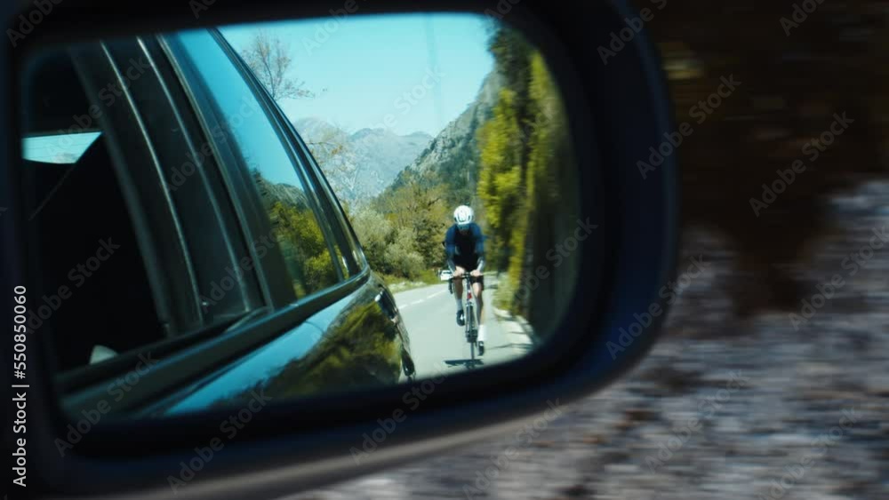Professional cyclist in car side view mirror cyclist rides on a mountain road Professional cyclist in car side view mirror cyclist rides on a mountain road