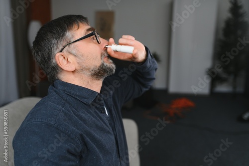 Portrait of man with a nasal spray. Sick man using nose drops while laying at the bed. Concept of treatment for allergies or the common cold, winter style. photo