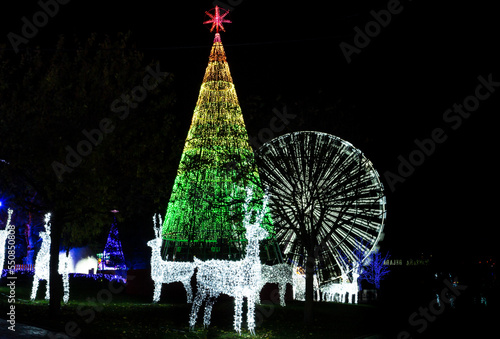 Christmas decoration set consisting of a Christmas tree, water with lights and a giant Ferris wheel. Christmas lights. Night photo of Christmas lights.