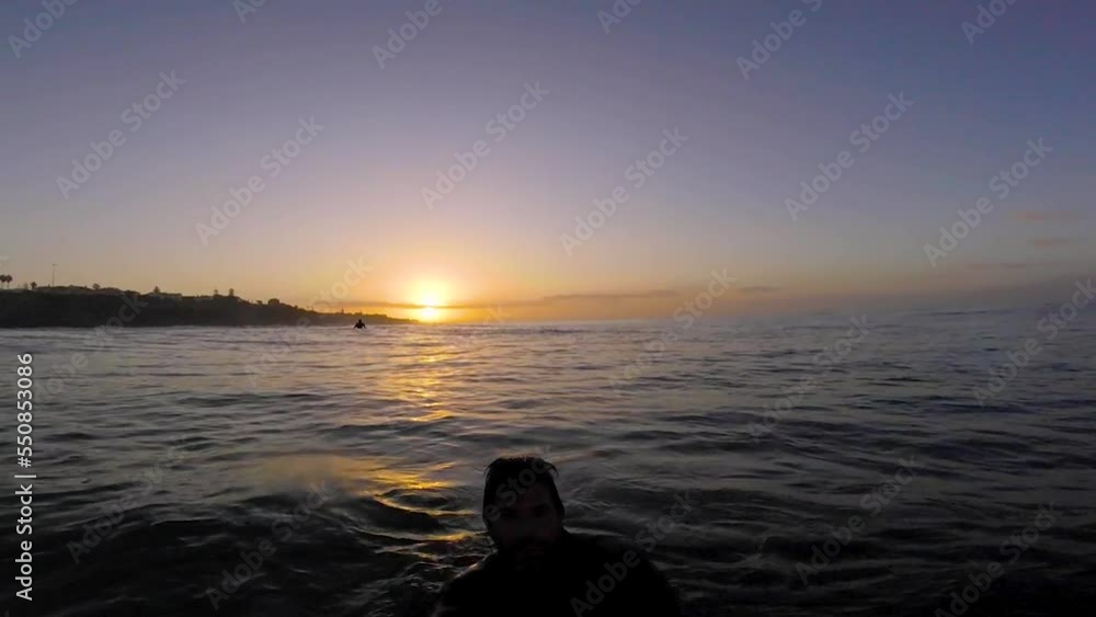Young man surfer sits on the line up during morning surf session, waits her wave and enjoys warm tropical sunrise Young man surfer sits on the line up during morning surf session, waits her wave and enjoys warm tropical sunrise