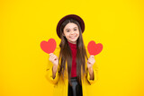 Happy teenager portrait. Cheerful lovely romantic teen girl hold red heart symbol of love for valentines day isolated on yellow background. Smiling girl.