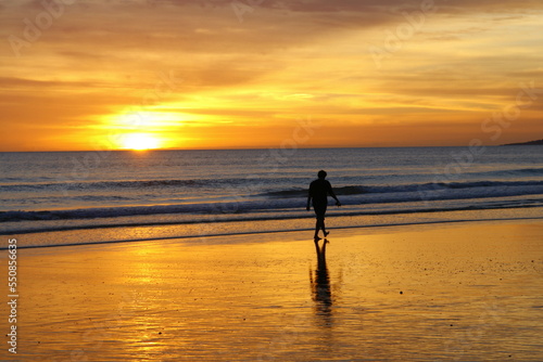 Un homme se promène sur une plage de l'Algarve au Portugal au coucher du soleil