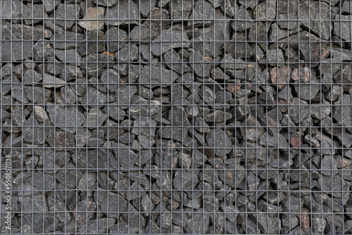 Modern privacy fence made of gabion galvanized steel grid with granite stones surrounding a residential building