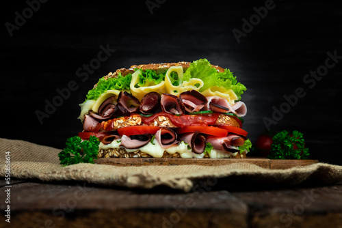 Sandwich with ham, salad, cheese and tomatoes on wooden rustick surface