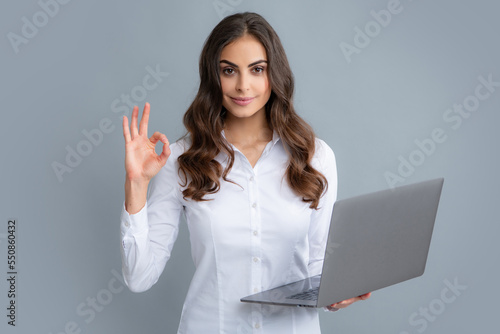 Cheerful business woman standing over grey wall with laptop computer. Portrait of pretty, charming, stylish, clever woman with open laptop chatting, using internet, isolated on grey background.