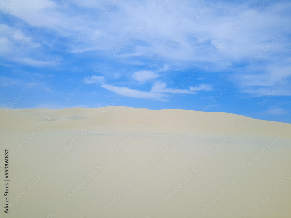Large white sand dune with blue sky and clouds in the background