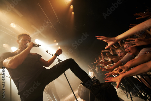 Band, singer and musician with fans, crowd and excited audience at concert, rock music festival and stage performance at nightclub. Man, artist and singing on mic at live show, event and techno party