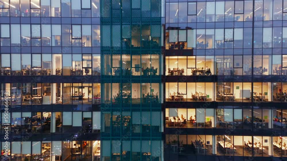 Aerial view of skyscraper windows at night. Drone shot along the facade of an office building close-up. People working in corporations and firms work overtime.