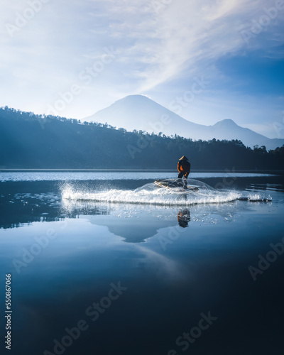 Traditional fishermen casting fishing nets in a lake with a mountain background located in Dieng, Central Java, Indonesia