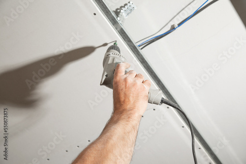 Worker with a drill screwdriver twists the screw into the drywall.